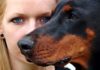 Primer plano de una mujer detrás de su perro. El hocico, por delante, cubre la mitad de su cara.