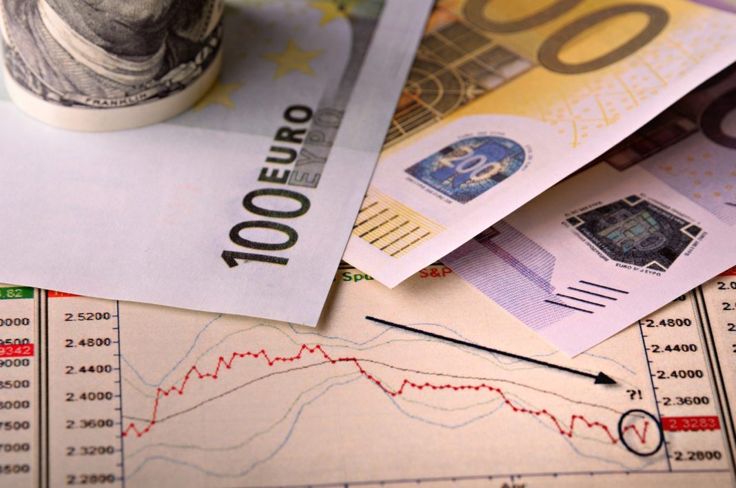 Billetes de cien y doscientos euros sobre una gráfica con una flecha que señala un descenso del valor.