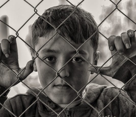 Niño en una verja, con cara triste