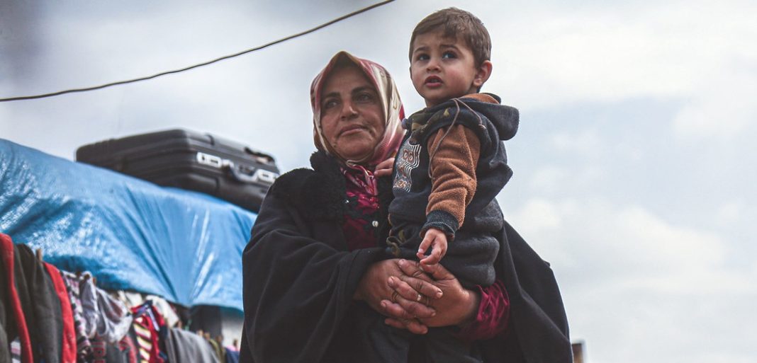 OCHA/Steve Hafez Una mujer viuda carga a su nieto en un campamento de desplazados en la provincia siria de Idlib