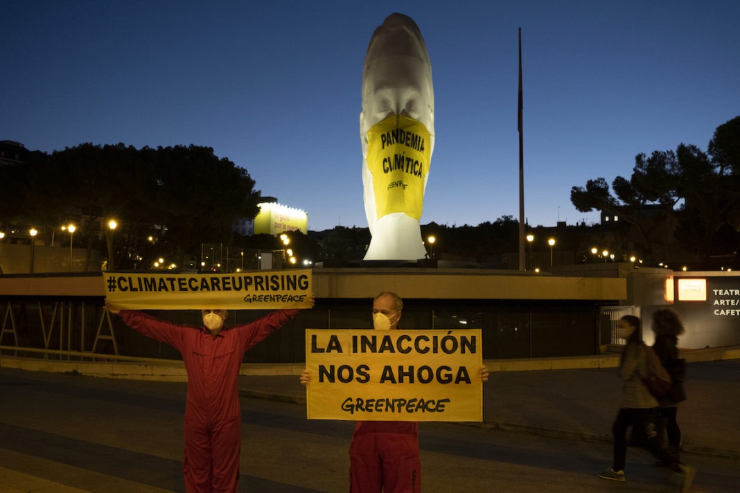Activistas de Greenpeace han colocado a primera hora de esta mañana una mascarilla gigante (4x5 metros) en una escultura de la plaza de Colón (Madrid) en la que se lee "Pandemia Climática". A su lado, otra pancarta señala "La inacción nos ahoga".