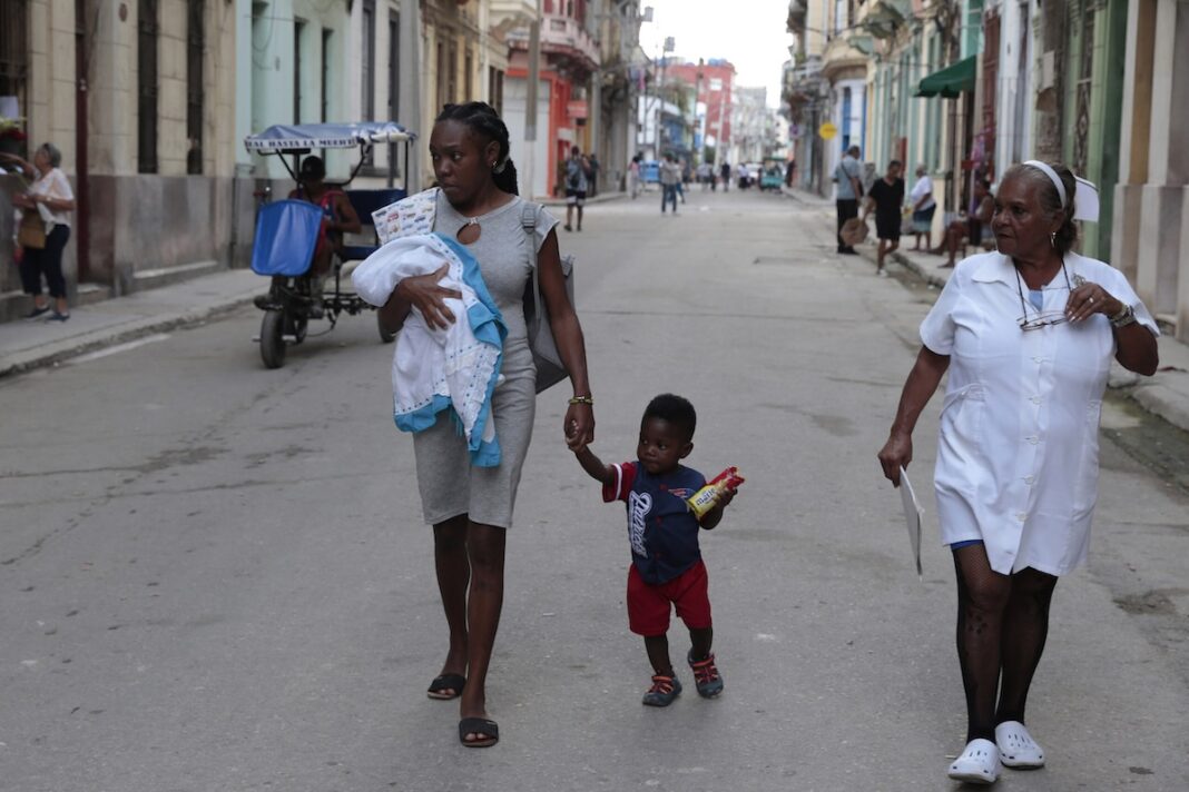 Cuba mujeres afrodescendientes ©Jorge Luis Baños : IPS Una madre afrodescendiente camina con su hijo de la mano y su pequeña bebe en brazos, cerca de una enfermera, por una calle céntrica de La Habana. ©Jorge Luis Baños / IPS