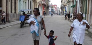 Una madre afrodescendiente camina con su hijo de la mano y su pequeña bebe en brazos, cerca de una enfermera, por una calle céntrica de La Habana. ©Jorge Luis Baños / IPS